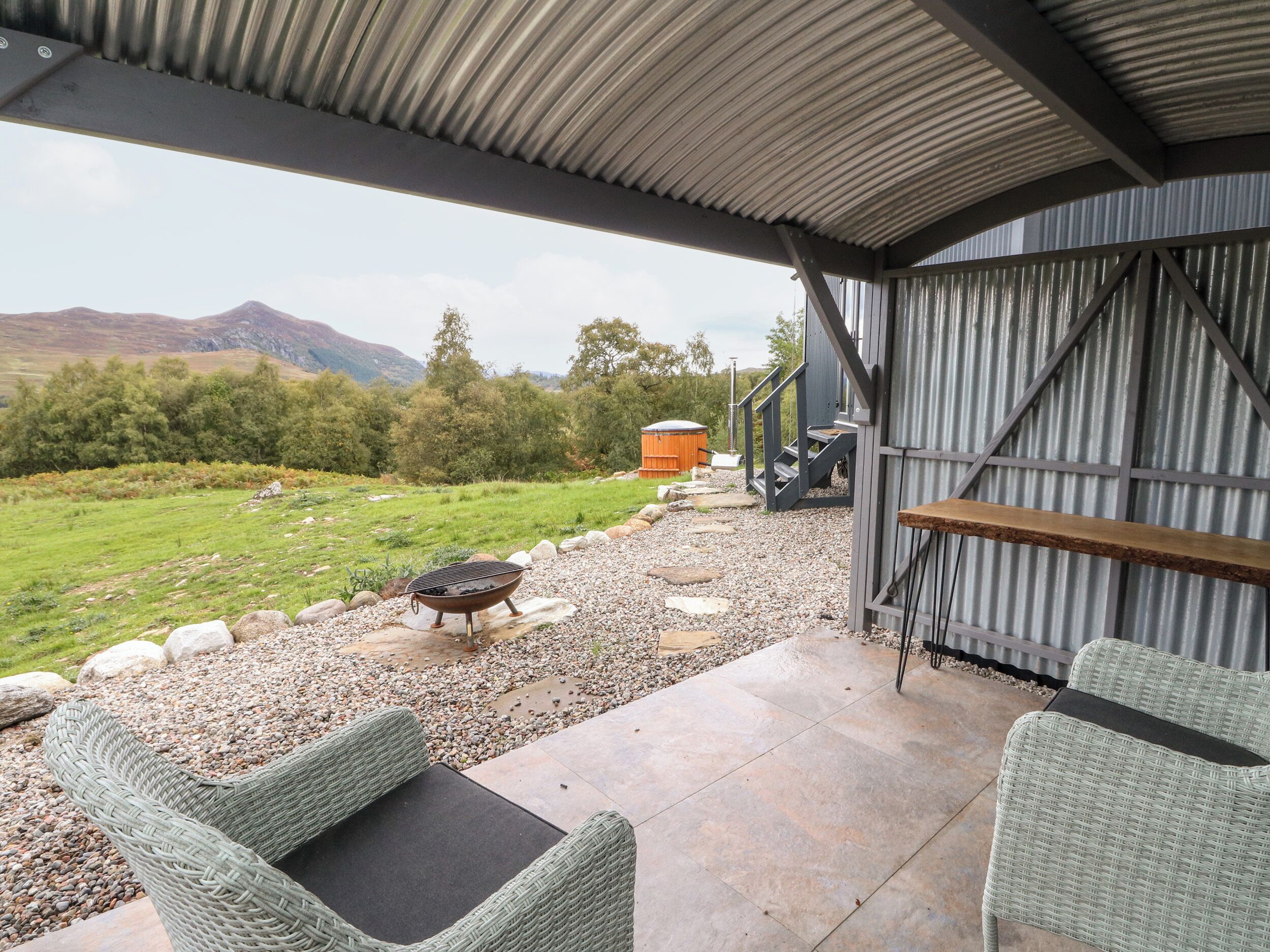 A covered patio area with wicker furniture, a fire pit, and a view of the surrounding landscape.