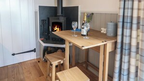 Ein gemütliches Zimmer mit Kaminofen, einem Holztisch mit zwei Gläsern und einer Bank.
