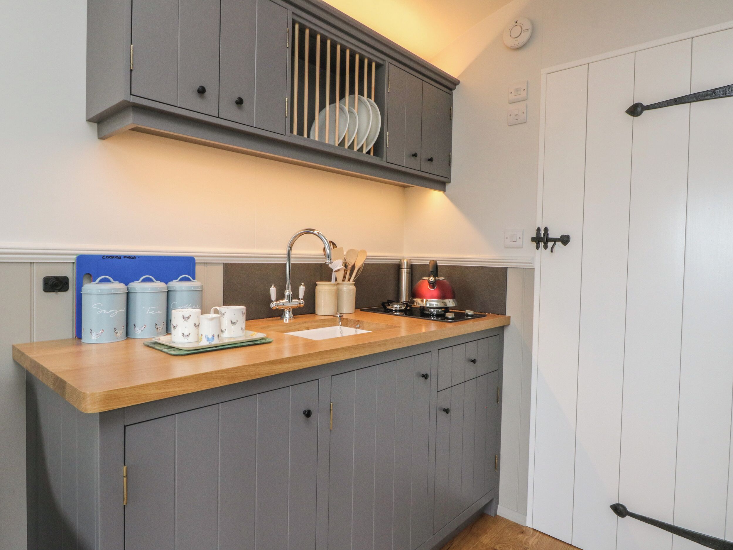 A kitchen with grey cabinets, a wooden countertop, a sink, and a stove. There are two blue storage containers on the counter.