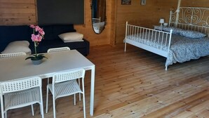 A wooden cabin room with a bed, a table with chairs, a mirror, and a small plant.