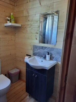 Een badkamer met houten lambrisering, een witte wastafel, donkere kastjes, een spiegel en een klein plankje met toiletartikelen.