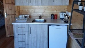 A compact kitchen with wooden cabinets, a sink, a small refrigerator, and a coffee maker.