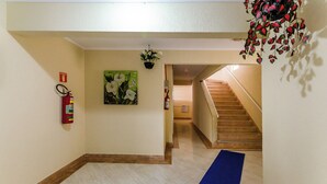 Pasillo de hotel con alfombra azul, suelo de madera, extintor, pintura floral verde y una escalera.