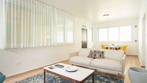 A modern living room with a sofa, a coffee table, and a dining area with yellow chairs.