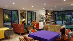 A restaurant with a variety of seating options, including tables and chairs, and a large bookshelf filled with books and bottles. - Hostelry (Écully)