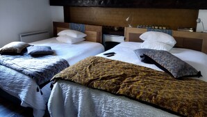A hotel room with two beds, each with white bedding and multiple pillows. The room has a wooden headboard and a small table with a lamp. - Hostelry (Écully)