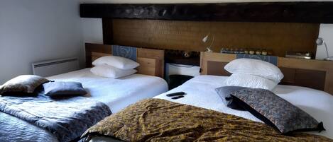 A hotel room with two beds, each with white bedding and multiple pillows. The room has a wooden headboard and a small table with a lamp.