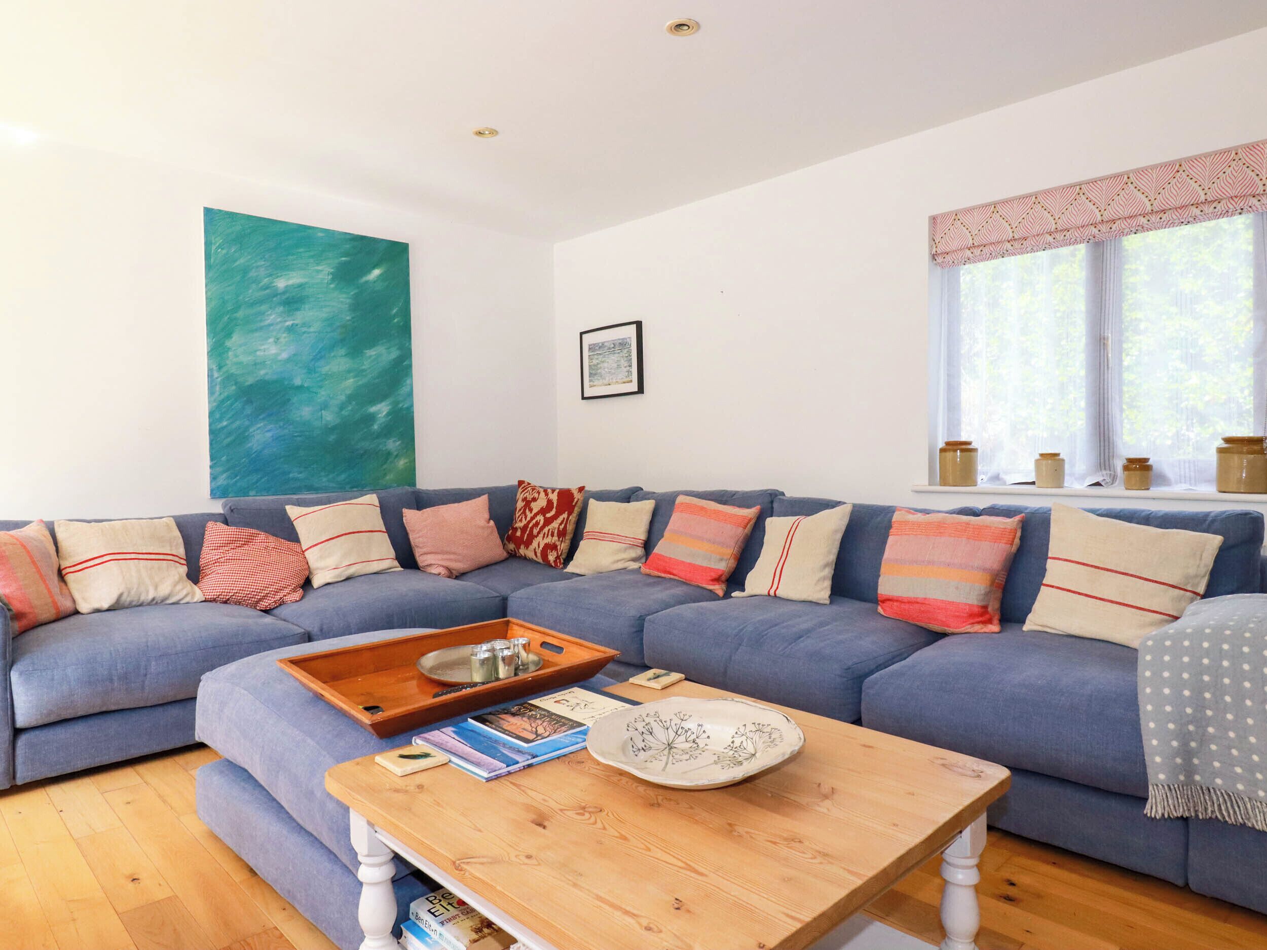 A living room with a blue sectional sofa, a wooden coffee table, and a large abstract painting on the wall.
