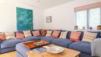 A living room with a blue sectional sofa, a wooden coffee table, and a large abstract painting on the wall.