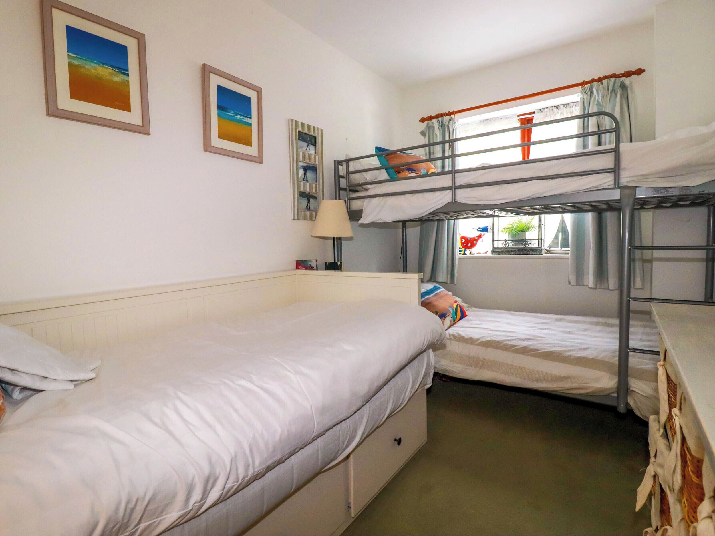 Une chambre de dortoir avec des lits superposés, un lit simple et deux tableaux encadrés au mur.