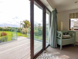 Una habitación con un gran ventanal corredera que da a una terraza de madera y vistas a un jardín.