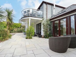 Una casa moderna con balcón, patio empedrado y mobiliario exterior.