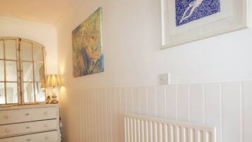 A room with a white dresser, a lamp, a radiator, and two framed artworks on the wall.