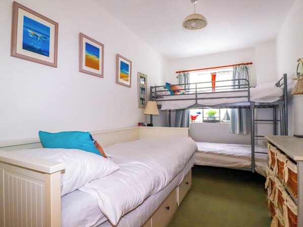A dormitory room with bunk beds, a single bed, a window with curtains, and framed pictures on the wall. - Goatsland (Wadebridge)