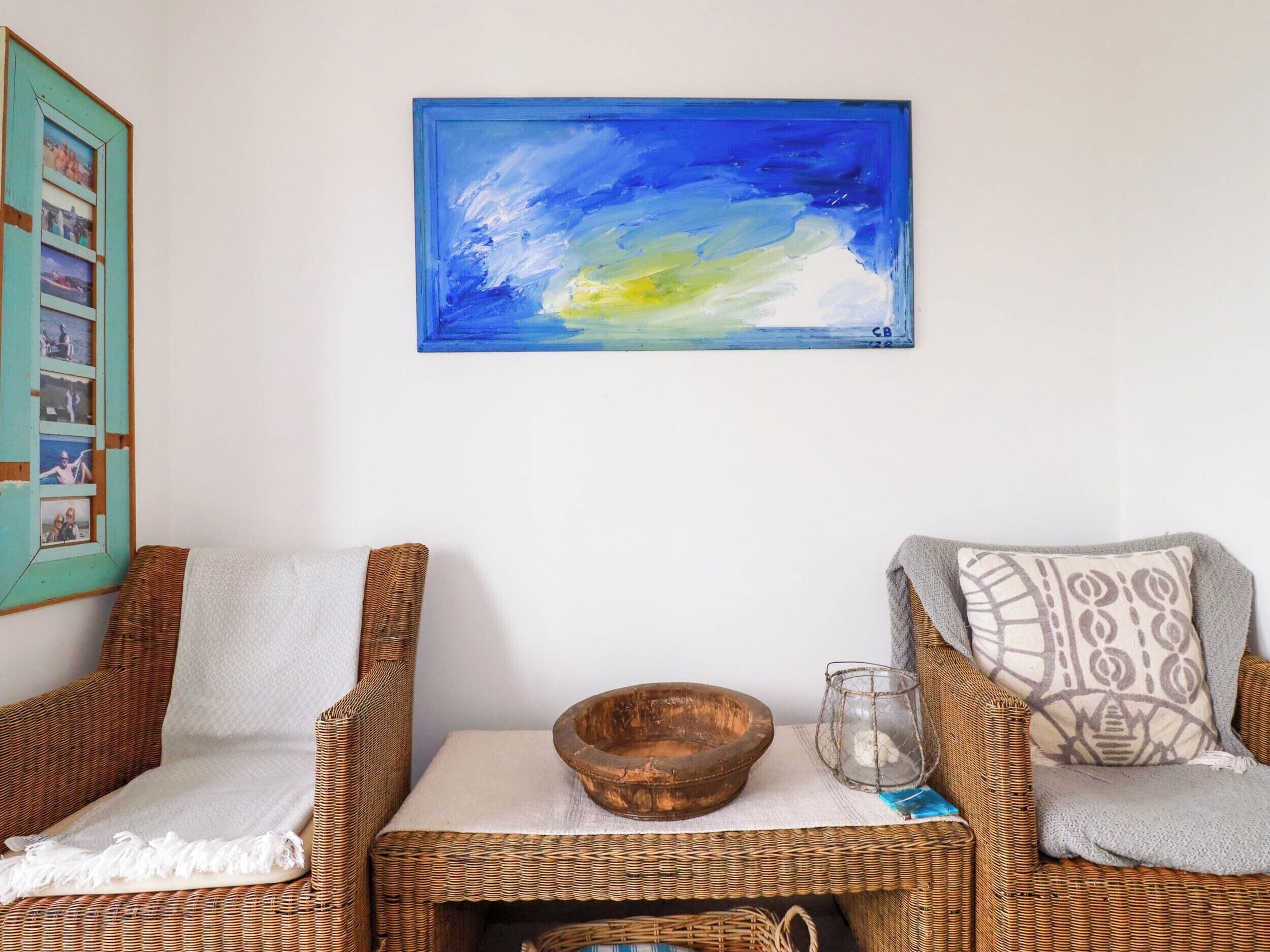Una habitación con dos sillones de mimbre, un cuenco de madera y un vaso sobre una mesita.