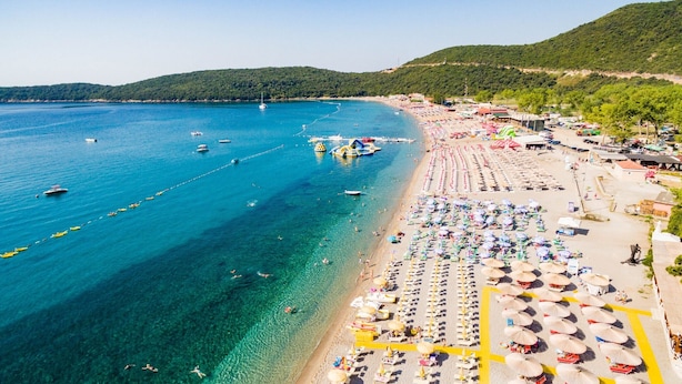Une plage avec une eau d’un bleu limpide, des rangées de transats et quelques bateaux.