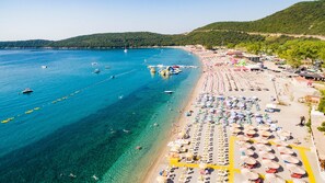 A beach with clear blue water, rows of sunbeds, and a few boats. - Beachfront Hotel Palma Jaz (Prijevor)
