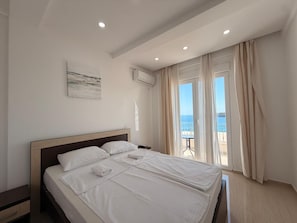 A hotel room with a large bed, a bedside table, an air conditioning unit, and a view of the sea. - Beachfront Hotel Palma Jaz (Prijevor)