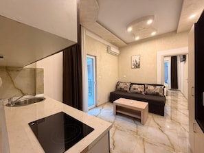 A modern kitchen with a built-in stove, a sink, and a marble countertop. There is a dark-colored sofa with patterned cushions in the living area. - Beachfront Hotel Palma Jaz (Budva)