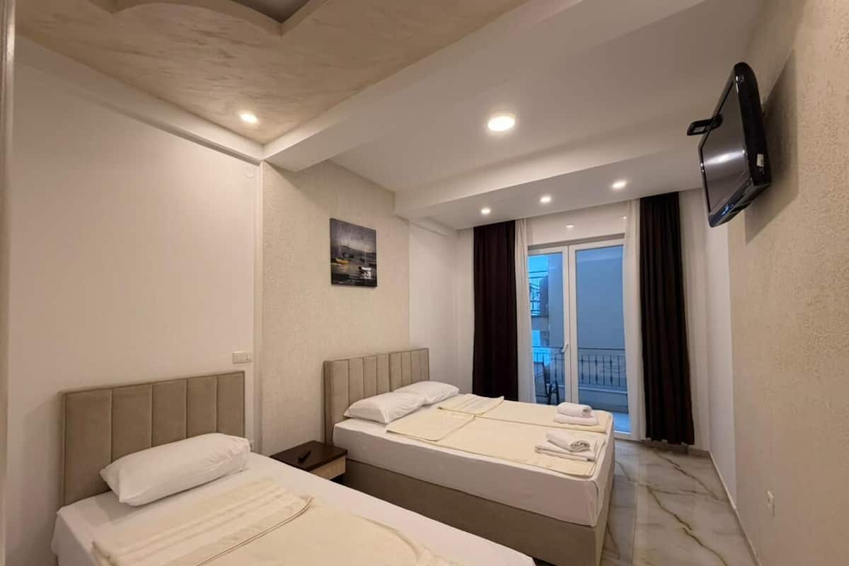 A hotel room with two beds, a flat-screen TV, a painting on the wall, and a view of the outside balcony.