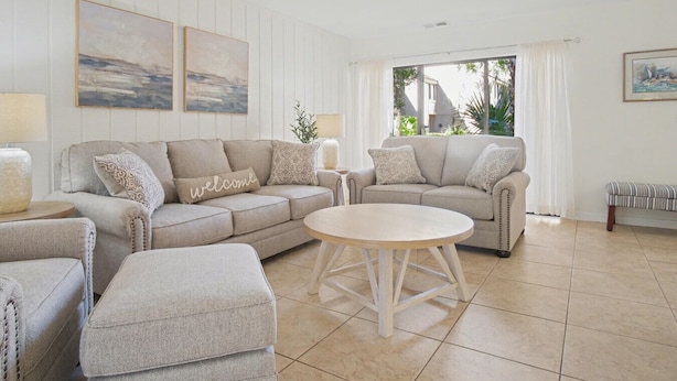 A modern living room with a beige sofa set, a round coffee table, and a bench.