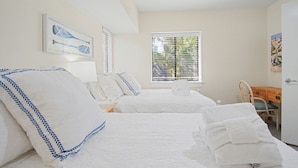 A hotel room with two beds, a desk, and a window with blinds.