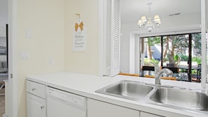 A kitchen with white cabinets, a double sink, and a window with a view of outdoor furniture.
