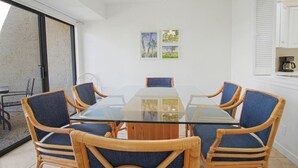 A dining area with a glass table surrounded by wicker chairs, a chandelier, and a view through a sliding glass door.