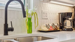 A modern kitchen with a stainless steel sink, a black faucet, a green vase with flowers, and a coffee maker. - Skyline Retreat 3br-3ba w Stunning Views Near DT (San Antonio)