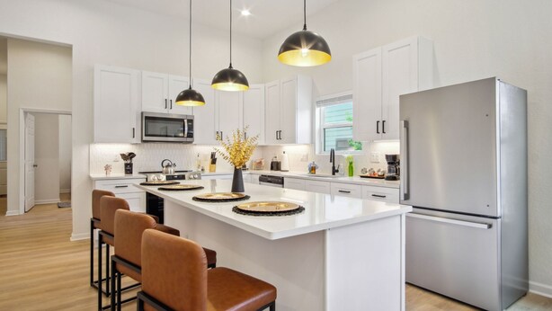 A modern kitchen with white cabinets, a stainless steel refrigerator, and pendant lighting. - Skyline Retreat 3br-3ba w Stunning Views Near DT (San Antonio)