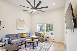 Ein modernes Wohnzimmer mit einem grauen Sofa, gelben Kissen, einem Couchtisch und einem Deckenventilator.