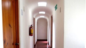 Un pasillo largo y estrecho con puertas de madera a un lado y un extintor en la pared.