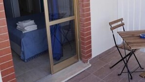 A room with a sliding glass door leading to a balcony, a small table with a chair, and a neatly made bed with a blue cover. - Casa Caretta Caretta a San Lorenzo (Noto)