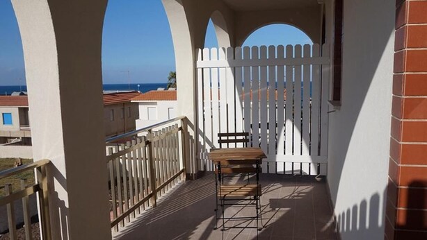 A balcony with a white picket fence, a wooden table, and a view of the sea. - Casa Caretta Caretta a San Lorenzo (Noto)