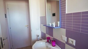A bathroom with a white sink, purple tiles, a mirror, and a door. - Casa Caretta Caretta a San Lorenzo (Noto)