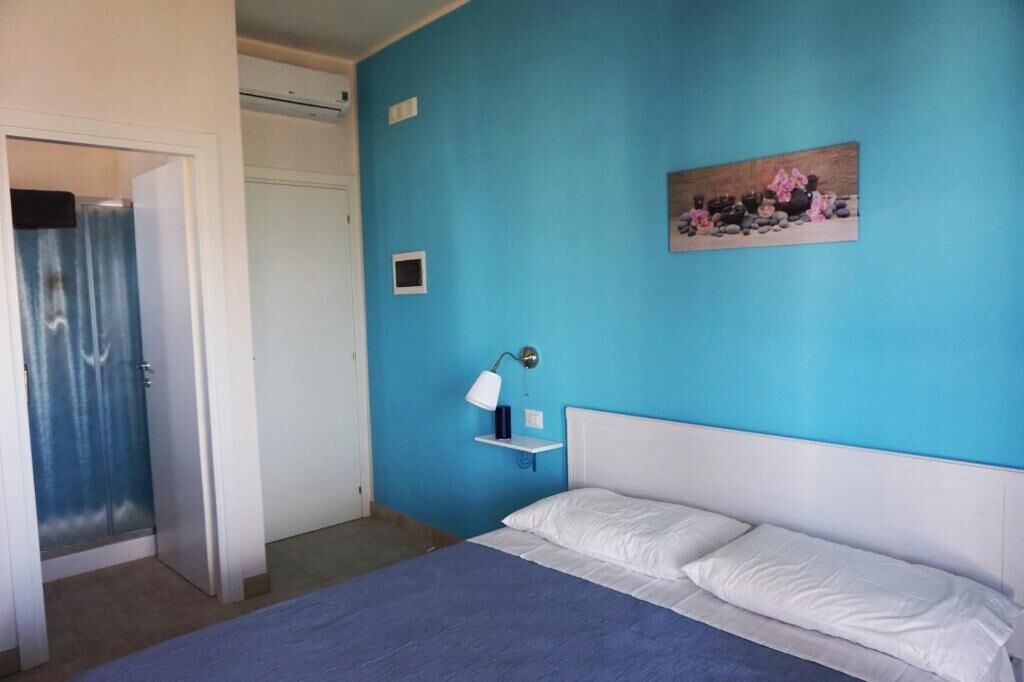 A bedroom with a bed, a nightstand, a wall-mounted lamp, and a painting.