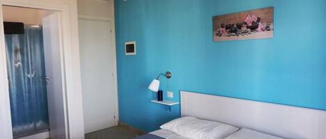 A bedroom with a bed, a nightstand, a wall-mounted lamp, and a painting.