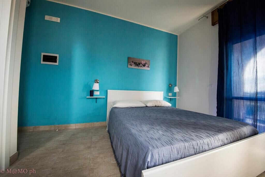 Un dormitorio con pared azul, cama blanca y una mesita de noche con lámpara.