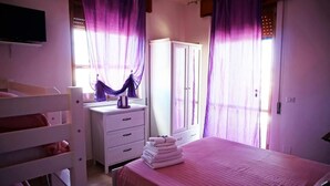 A bedroom with a bed, a desk, a wardrobe, and purple curtains. - Casa Caretta Caretta a San Lorenzo (Noto)