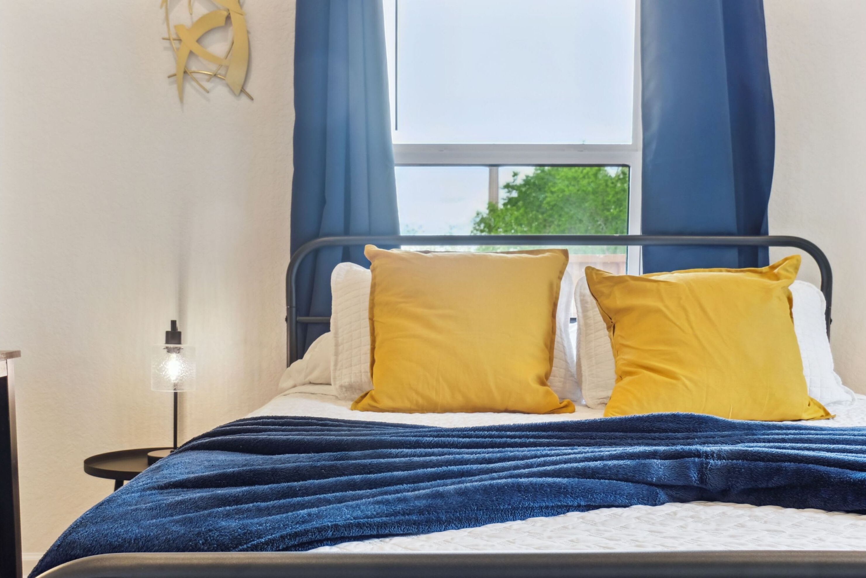 Un lit bien fait, avec une couverture bleue, deux oreillers jaunes et une lampe de chevet.
