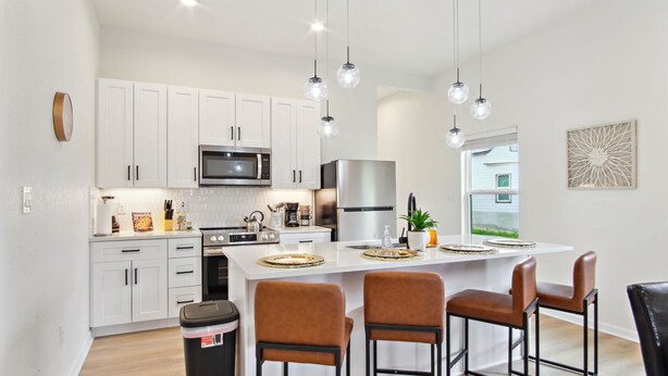 A modern kitchen with white cabinets, stainless steel appliances, and a central island with bar stools. - 3br-2ba Cityscape Haven With Panoramic Tower View (San Antonio)