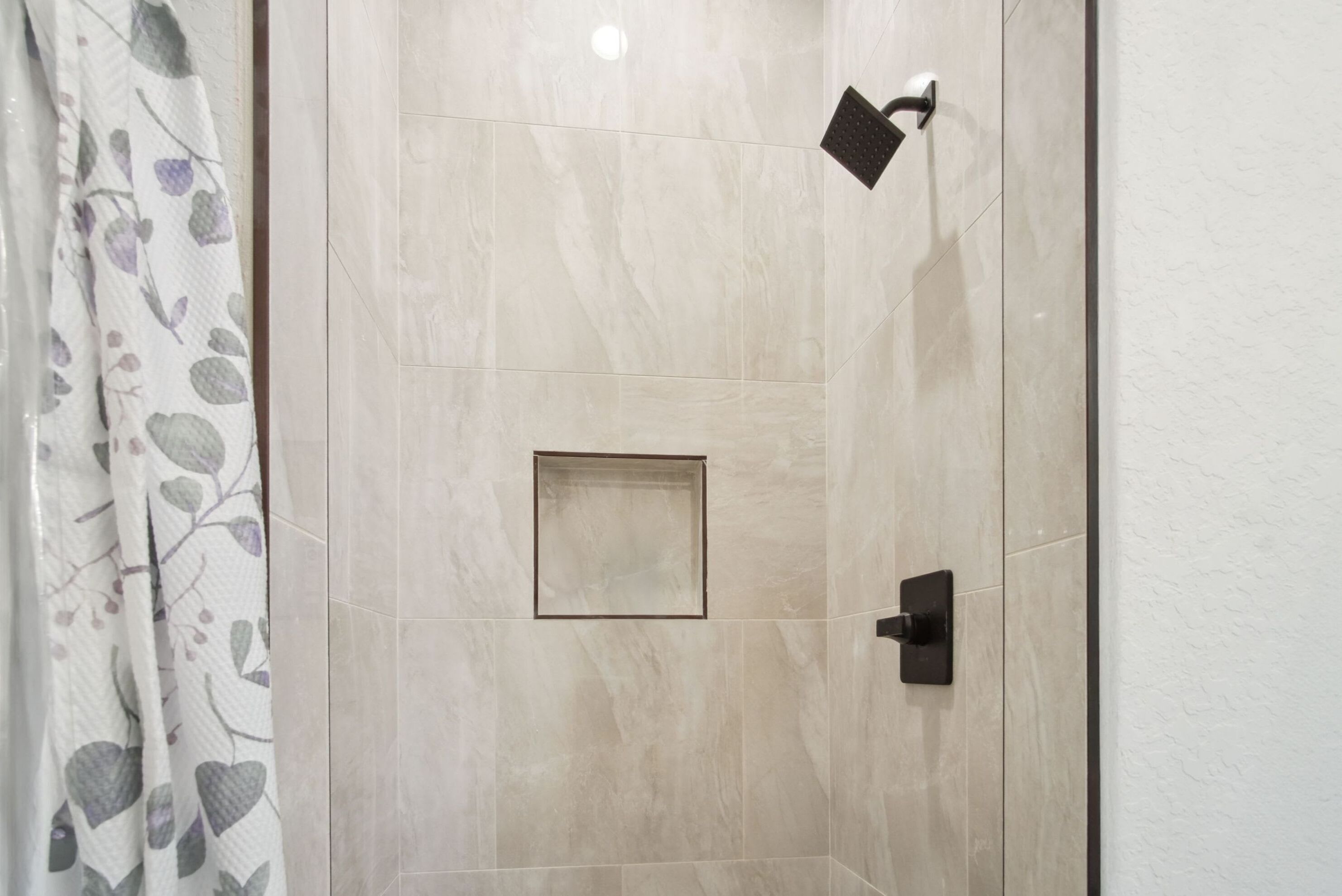 A shower area with a tiled wall, a showerhead, and a door with a handle.