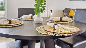 A round dining table with woven placemats, white napkins, and a white vase with green foliage. - 3br-2ba Cityscape Haven With Panoramic Tower View (San Antonio)