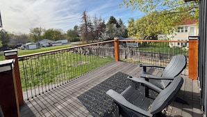 A deck with a wooden railing, outdoor seating, and a view of a grassy yard with trees and a house in the background. - Welcome to the Raven Rose - A Chic, Newly Renovated 2BD/1BA Home (Logan)