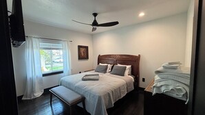 A bedroom with a bed, a ceiling fan, a window with curtains, a bedside table, and a stack of towels. - Welcome to the Raven Rose - A Chic, Newly Renovated 2BD/1BA Home (Logan)