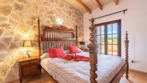 Un dormitorio con pared de piedra, una cama con dosel de madera, una mesita de noche y una ventana con vistas.