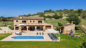 Una casa de piedra de dos pisos con piscina, mobiliario de exterior y una zona de juegos para niños.