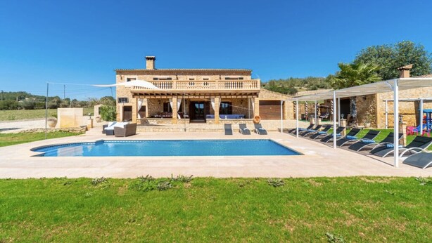 Una villa de piedra con piscina, mobiliario exterior y un porche cubierto.
