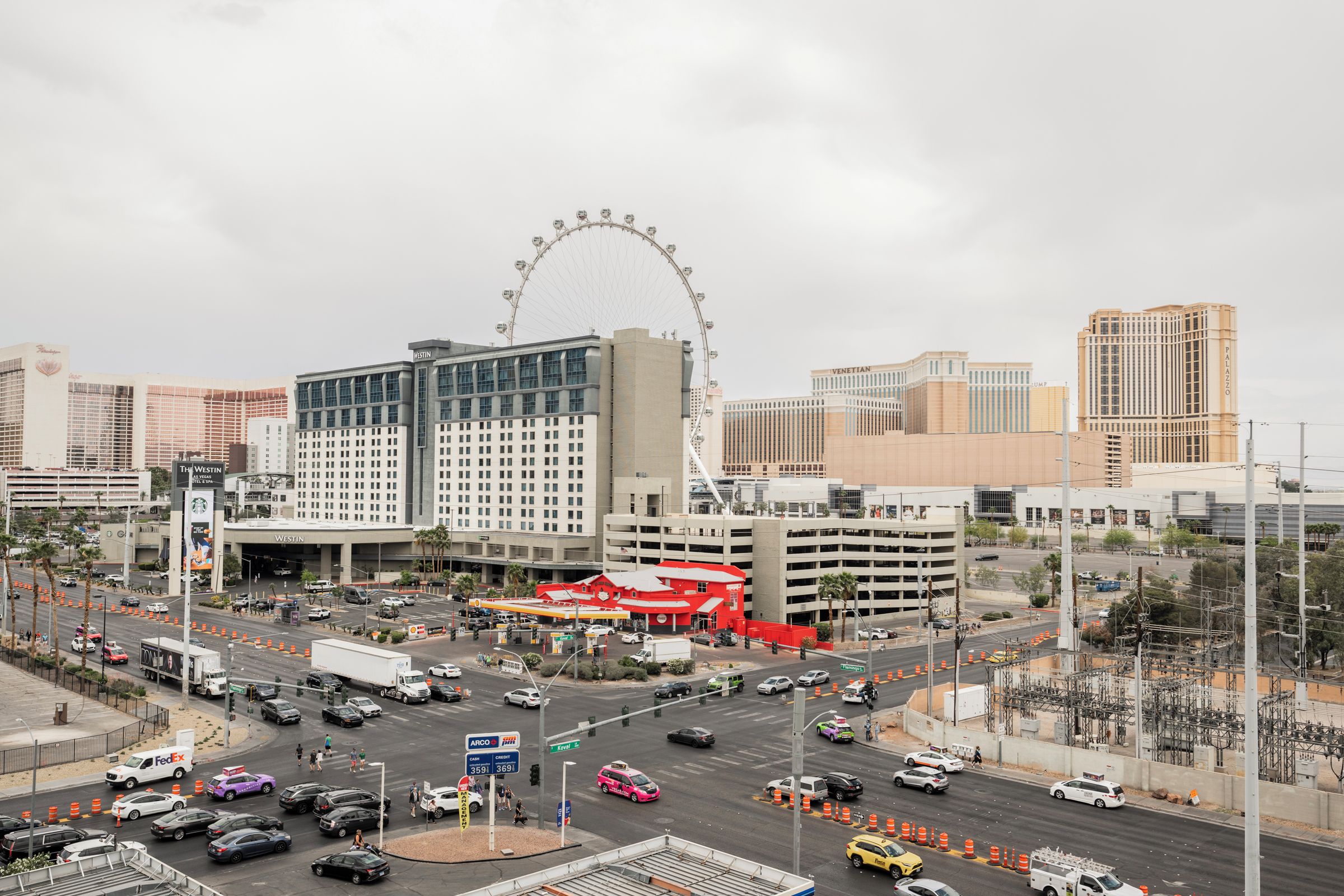 Une intersection animée, avec une grande roue bien visible en arrière-plan, entourée d’immeubles de grande hauteur et d’un grand hôtel reconnaissable à son toit rouge distinctif.