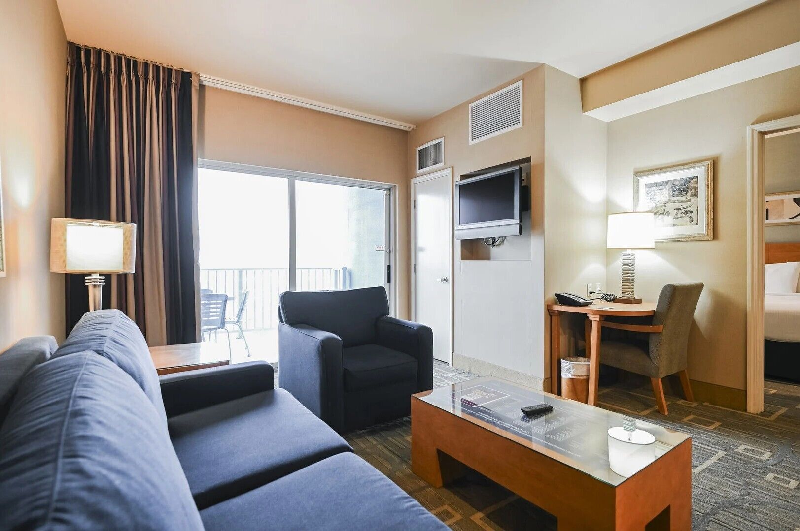 Habitación de hotel con sofá, sillón, mesa de centro, televisor y escritorio con silla.